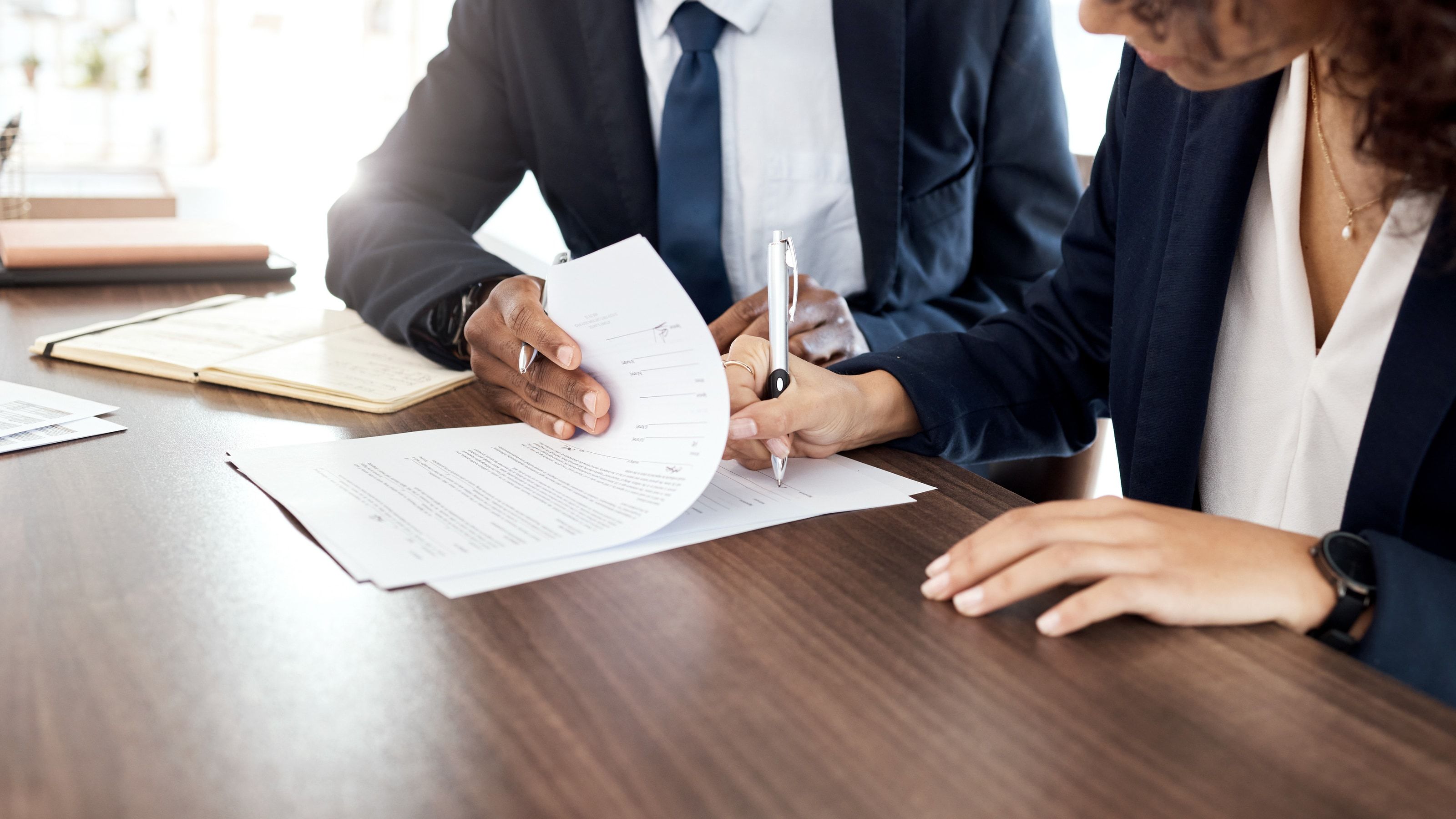 Manos firmando un contrato legal sobre una mesa de despacho